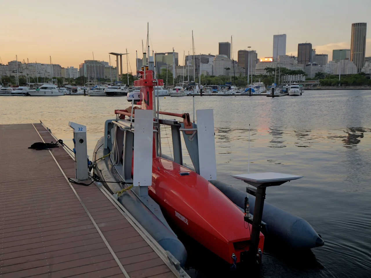 USV Exail DriX amarrado ao lado de um pier flutuante, com a antena GNSS de popa e o mastro de comunicação.