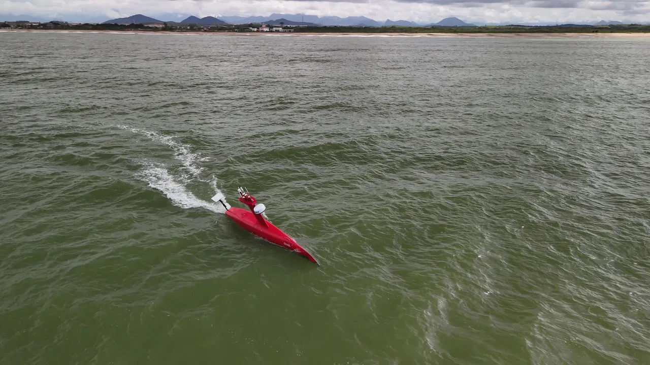 USV Exail DriX em deslocamento, visto do alto pelo drone, com a esteira na água.