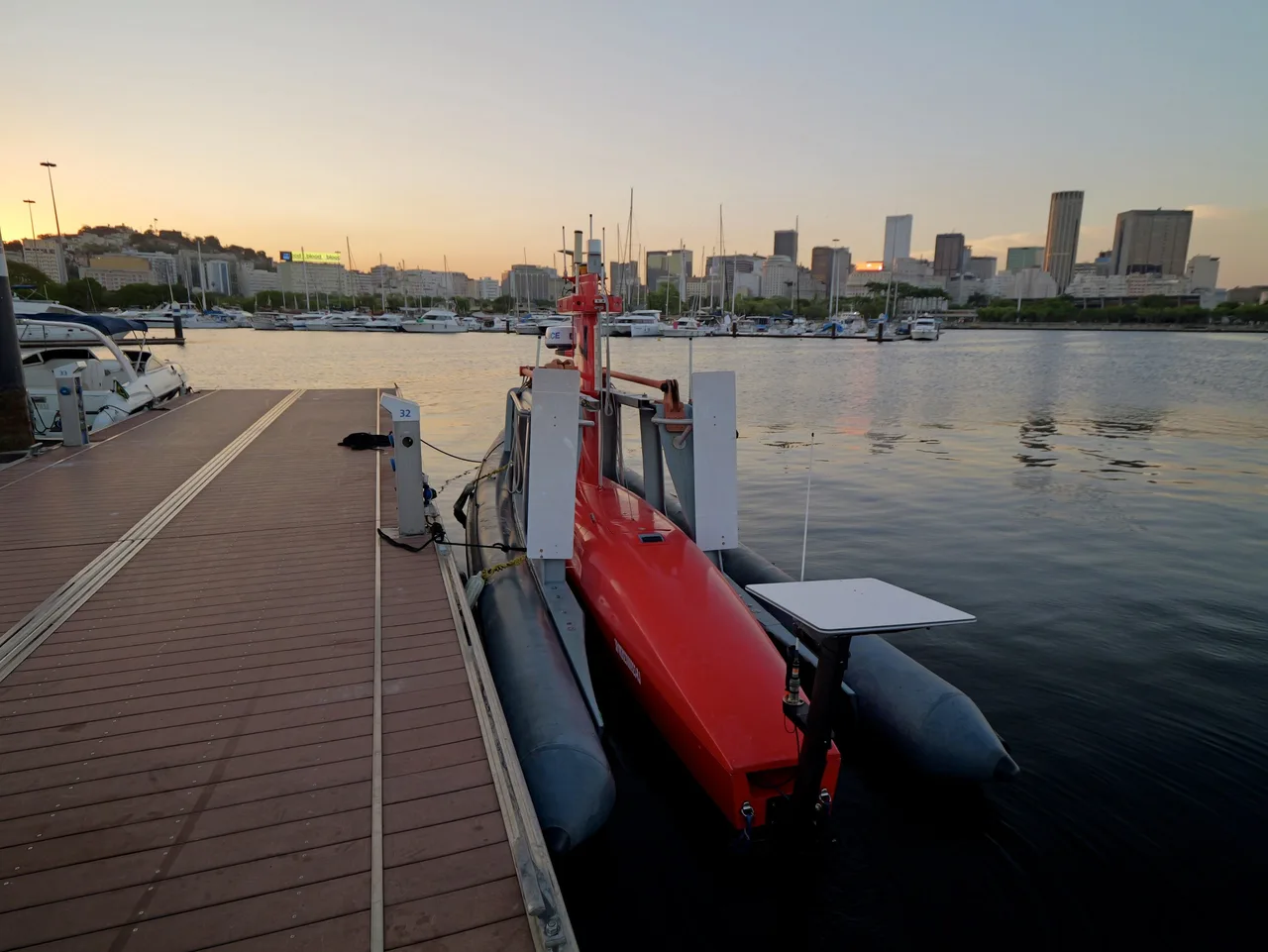 USV Exail DriX atracado a um pier flutuante ao entardecer, visto de cima e de popa.