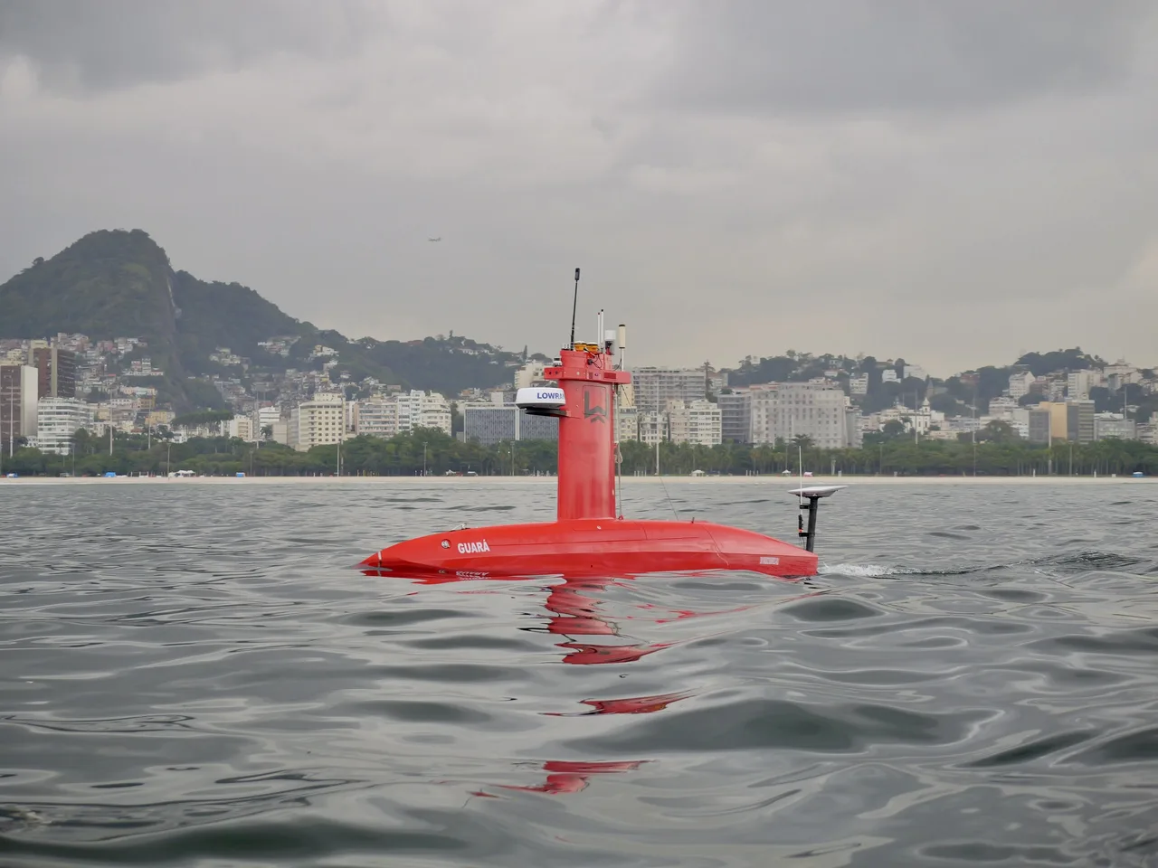 USV Exail DriX em águas calmas na Baía de Guanabara, com morro e prédios ao fundo.