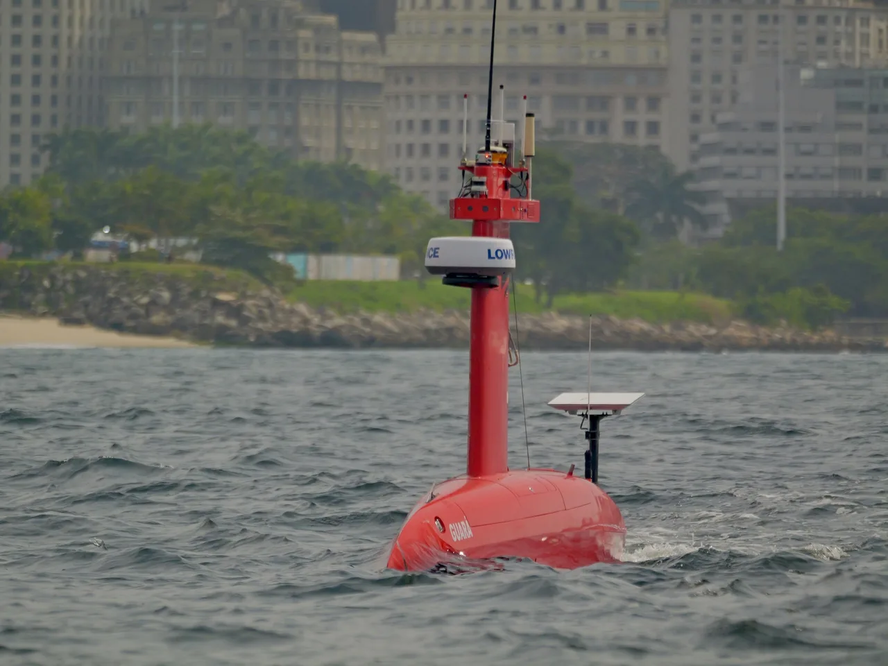 USV Exail DriX em navegação na Baía de Guanabara, visto de frente, com prédios da orla ao fundo.