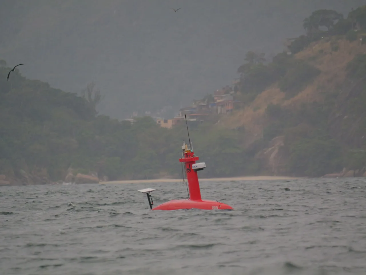 USV Exail DriX navegando junto a uma encosta com vegetação na Baía de Guanabara.