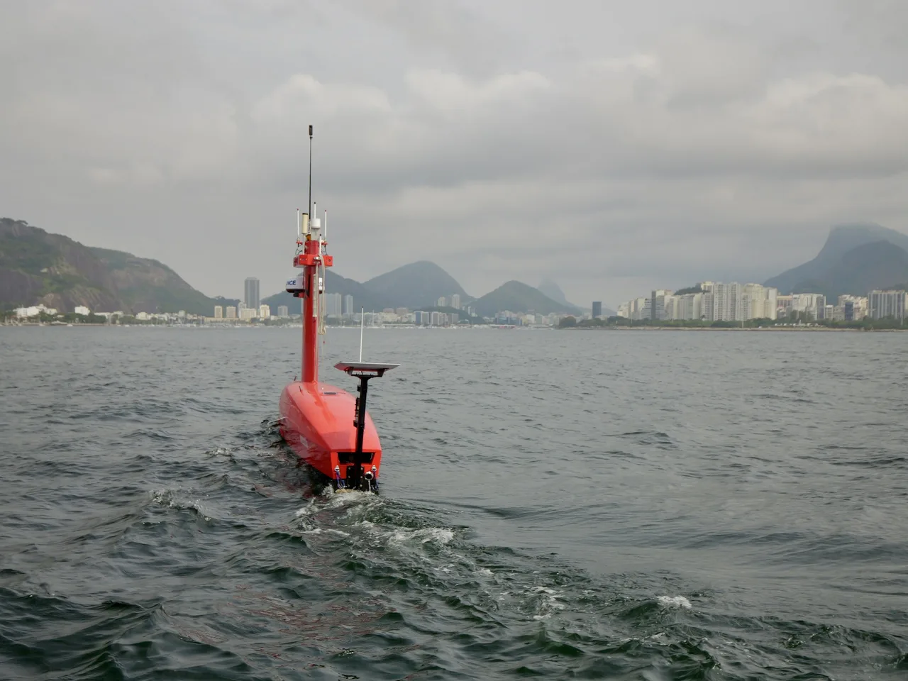 USV Exail DriX visto de popa em linha de levantamento na Baía de Guanabara, com a esteira na água.