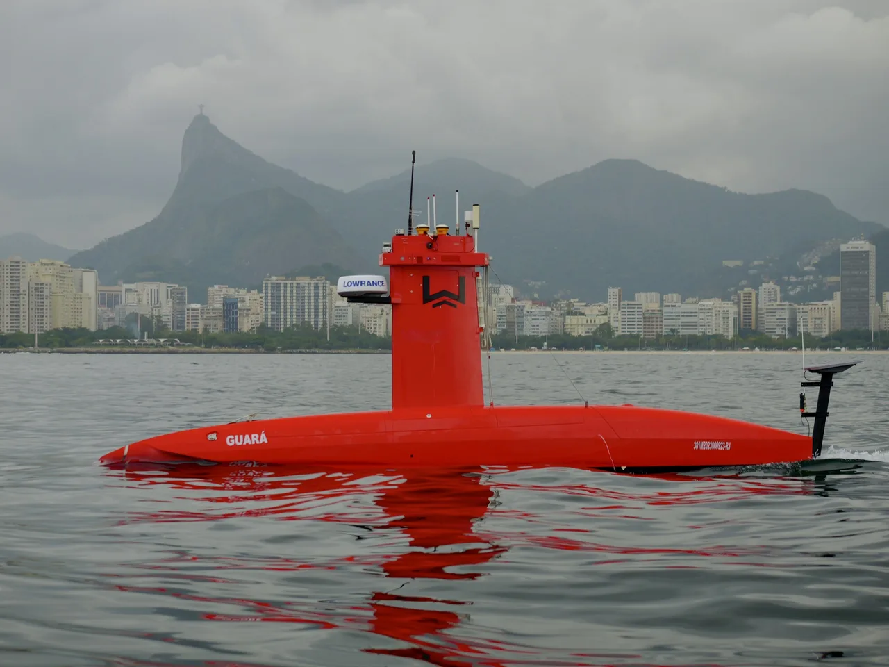 USV Exail DriX em navegação na Baía de Guanabara, visto de frente, com morros e prédios da orla ao fundo.